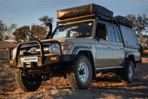 Toyota LandCruiser 70 Series wagon on red dirt outback track at golden hour, fitted with bull bar, snorkel and roof tent